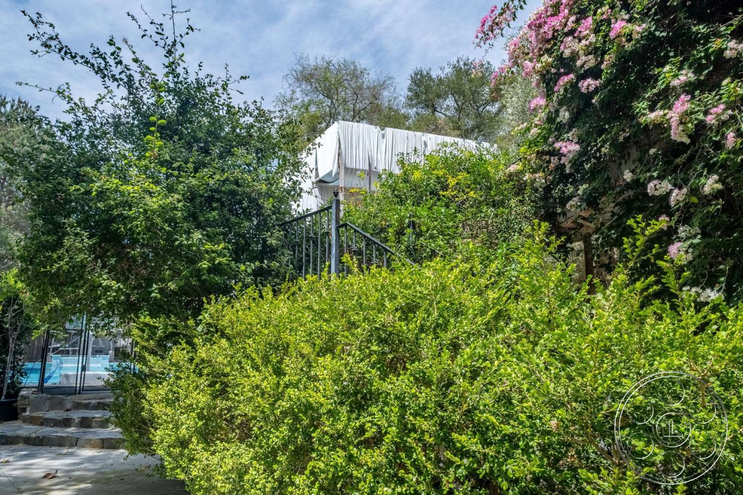 French 29 - exterior, modern architectural style, colorful flowering plants, wooden privacy fence, stepping stone pathway, lush green landscaping, bushy hedges, metal railing stairs, in-ground swimming pool background