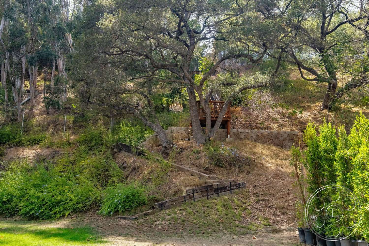 French 29 - exterior, patio area, sloping terrain, scenic hillside, natural stone retaining wall, lush green landscaping, grassy lawn area, wooden garden deck, dense tree cover, bushes and low shrubs