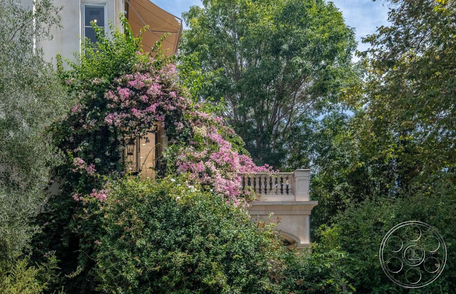French 29 - exterior, landscaped garden, lush greenery backdrop, plaster wall finish, two-story home, tropical garden setting, stone balcony railing, bougainvillea climbing plants, detailed architectural trim, wooden eaves