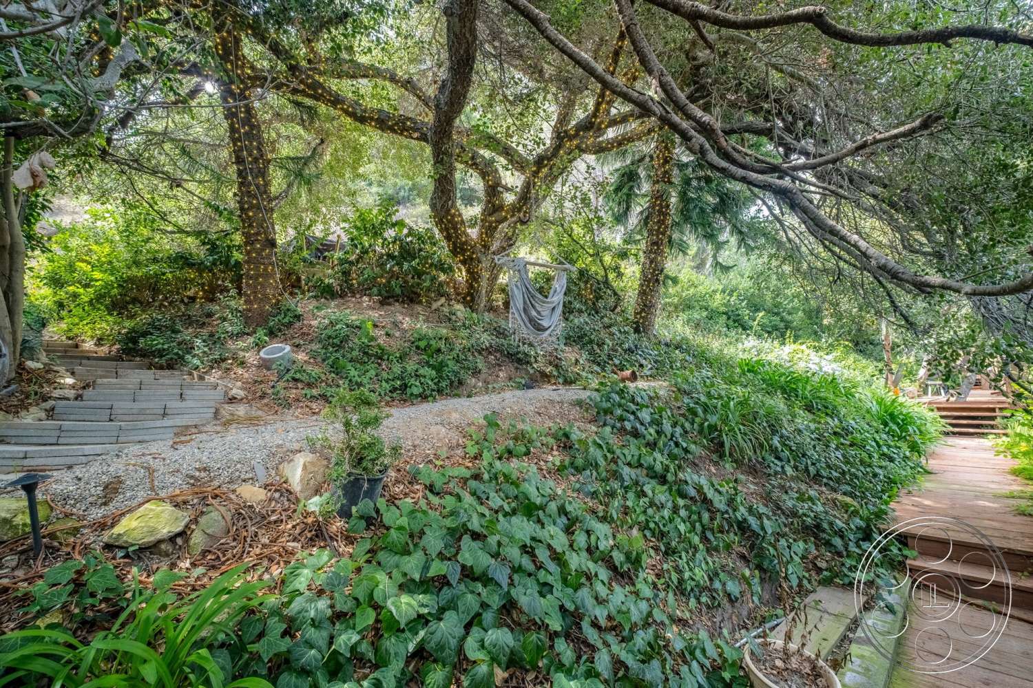French 29 - landscaped garden, wooden deck, wooden pathway, natural stone steps, leafy trees, gravel garden path, exterior garden setting, dense greenery, outdoor hammock area, steps leading to garden, lush plant beds