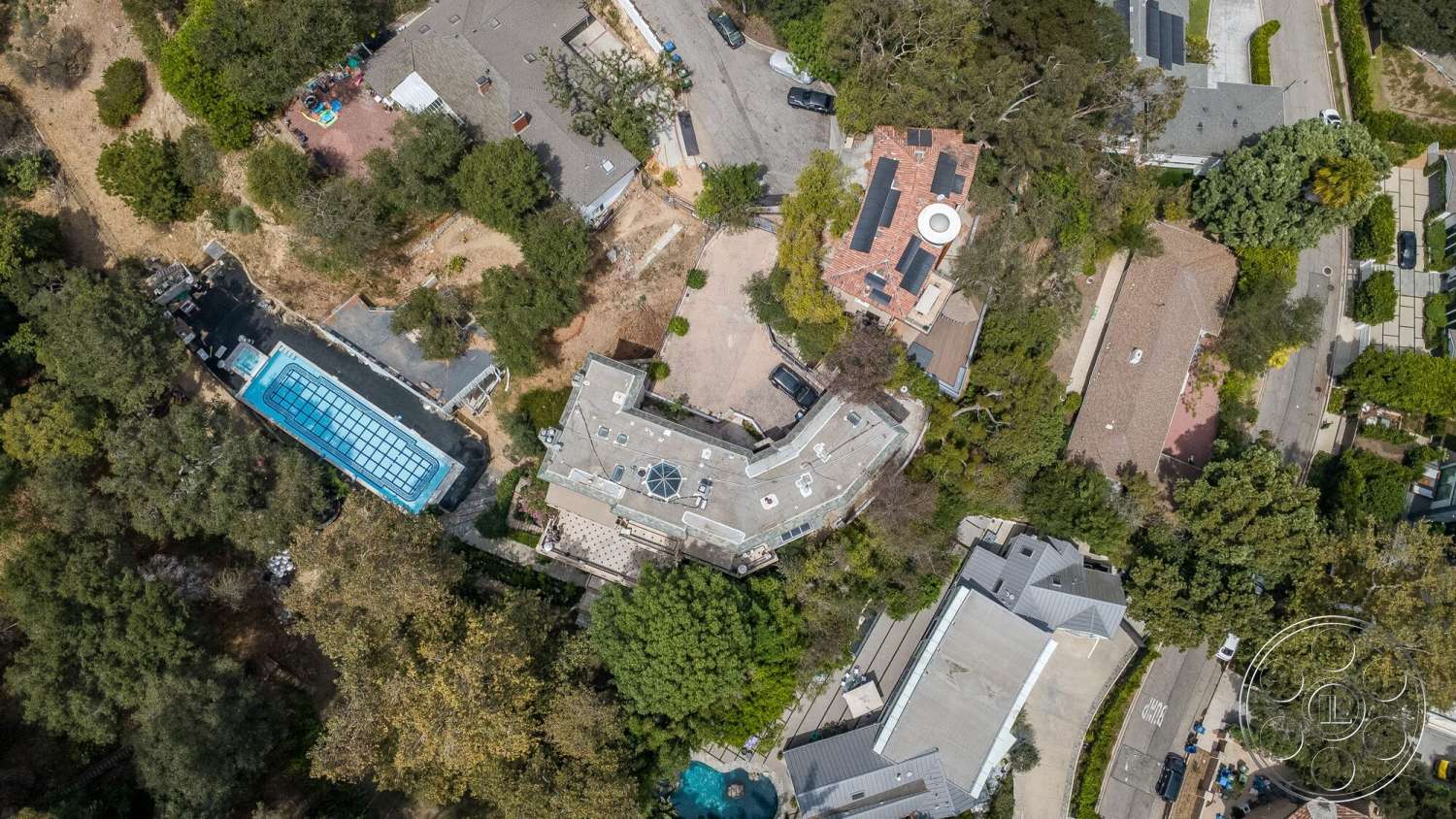 French 29 - exterior, surrounding greenery, asphalt driveway, concrete pool deck, urban residential setting, two-story home, solar panels on roof, landscaped garden with trees, brick exterior wall, in-ground rectangular swimming pool, tile roof on house, sloped backyard