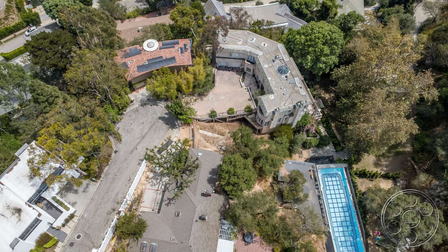 French 29 - exterior, flat roof, wooden deck, curved pathway, rectangular swimming pool, surrounding trees, solar panels, red tile roof, stone driveway, brick exterior, two-story home, concrete patio area, landscaped garden patio, vaulted entrance