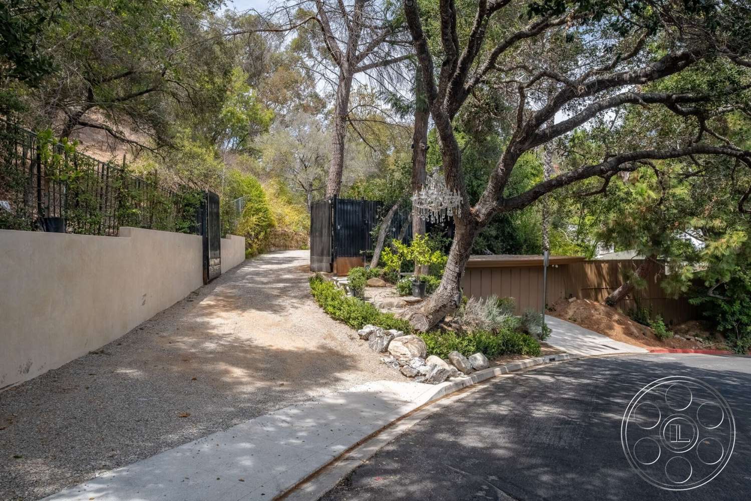 French 29 - seasonal foliage, mature trees, tropical landscaping, stucco walls, gravel driveway, wooden gate, stone garden border, curved asphalt road, decorative chandelier hanging from tree