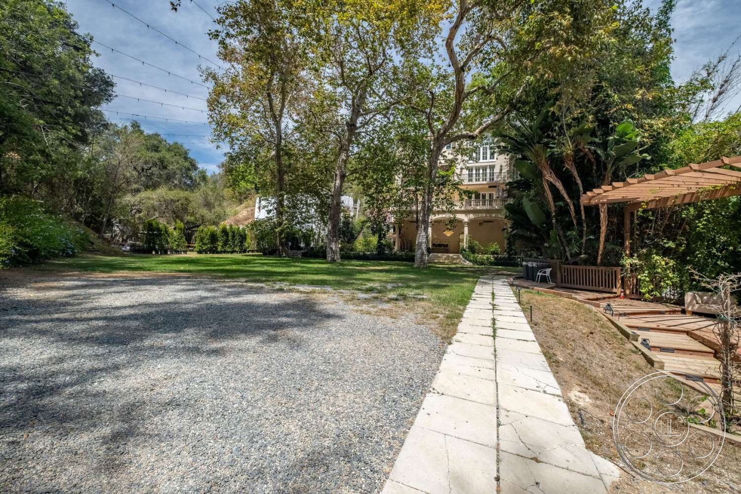 French 29 - exterior, landscaped garden, outdoor seating area, mature trees, stone pathway, lush green lawn, residential backyard, gravel driveway, wood pergola, dining patio, stone foundation