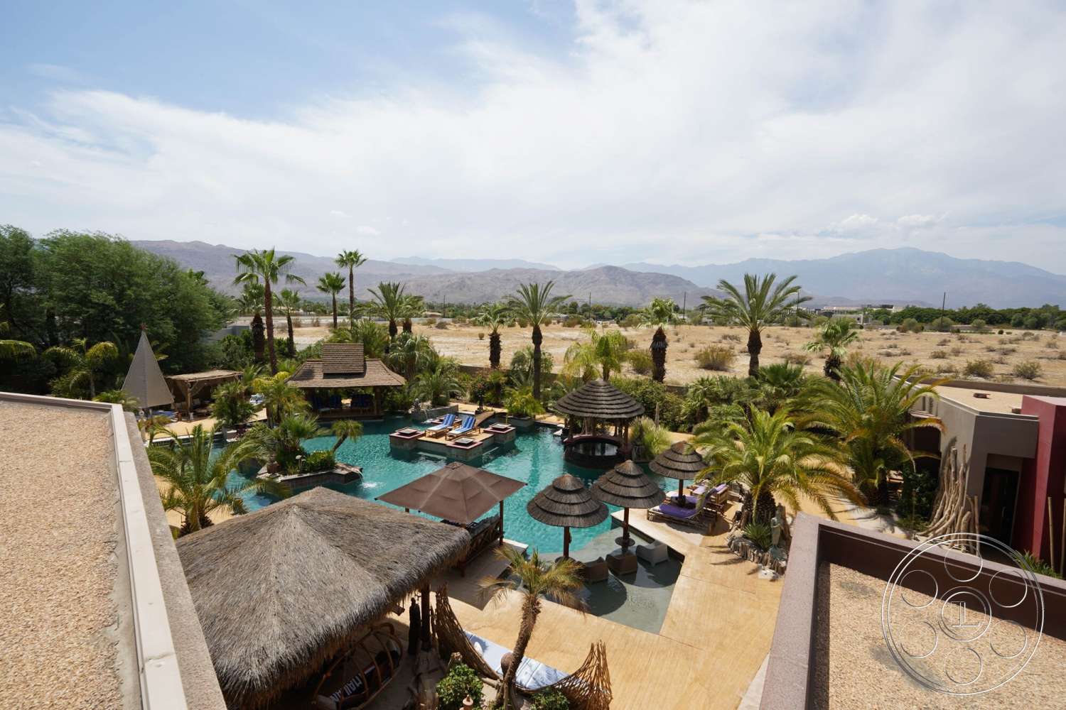 Rancho Mirage 4 - exterior, textured concrete walls, stone pathway, thatched roof cabana, tropical garden, outdoor dining space, rectangular pool, wooden lounge chairs, desert setting, open-air seating area, concrete patio flooring, palm tree landscaping, mountain view backdrop, sunken lounge area, sunshade structure