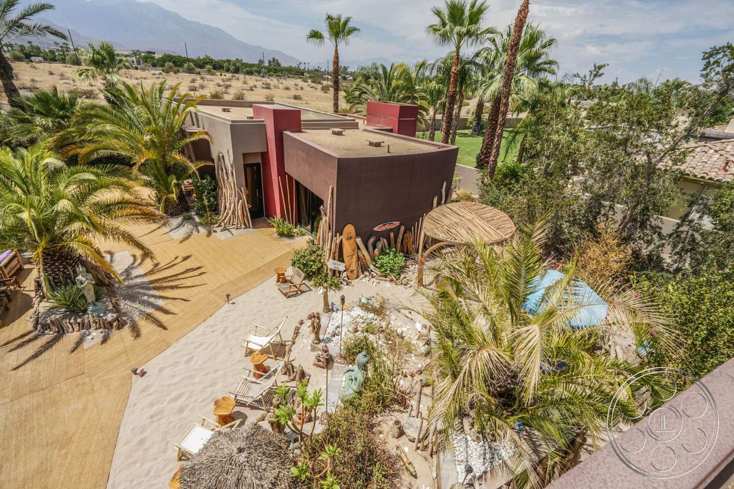 Rancho Mirage 4 - exterior, flat roof, palm trees, earthy color palette, outdoor seating area, landscaped yard, desert landscape, stucco walls, drought-tolerant plants, wood deck flooring, organic garden elements, sand patio, curved wooden structure, modern avant-garde design, stone decorative features