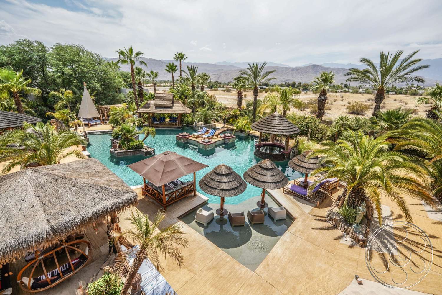 Rancho Mirage 4 - exterior, concrete patio, desert landscape, thatched roof cabana, infinity pool, wooden lounge chairs, stone pool deck, wood deck flooring, palm tree landscaping, stone water feature, resort-style outdoor setting, tropical garden patio