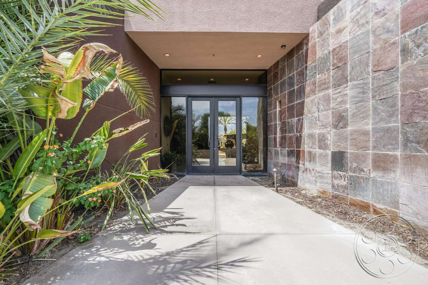Rancho Mirage 4 - exterior, low-maintenance plants, tropical landscaping, smooth concrete pathway, natural light entryway, modern glass entry doors, slate stone accent wall, neutral stucco wall finish, spacious front entrance