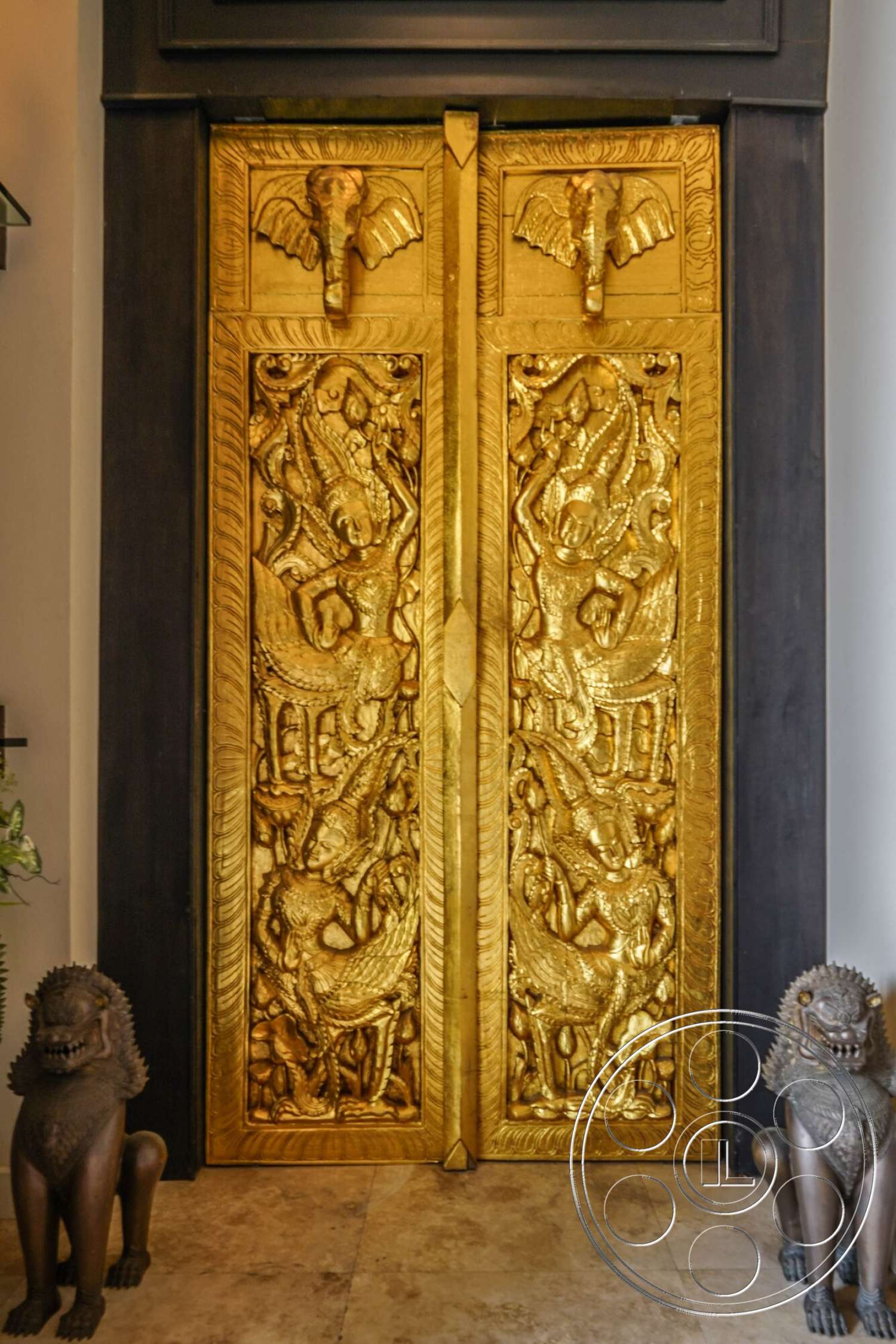 Rancho Mirage 4 - dark wood door frame, interior entrance, gold leaf door panels, intricately carved reliefs, elephant door handles, textured stone floor tiles, Asian-inspired architectural details, lion statues