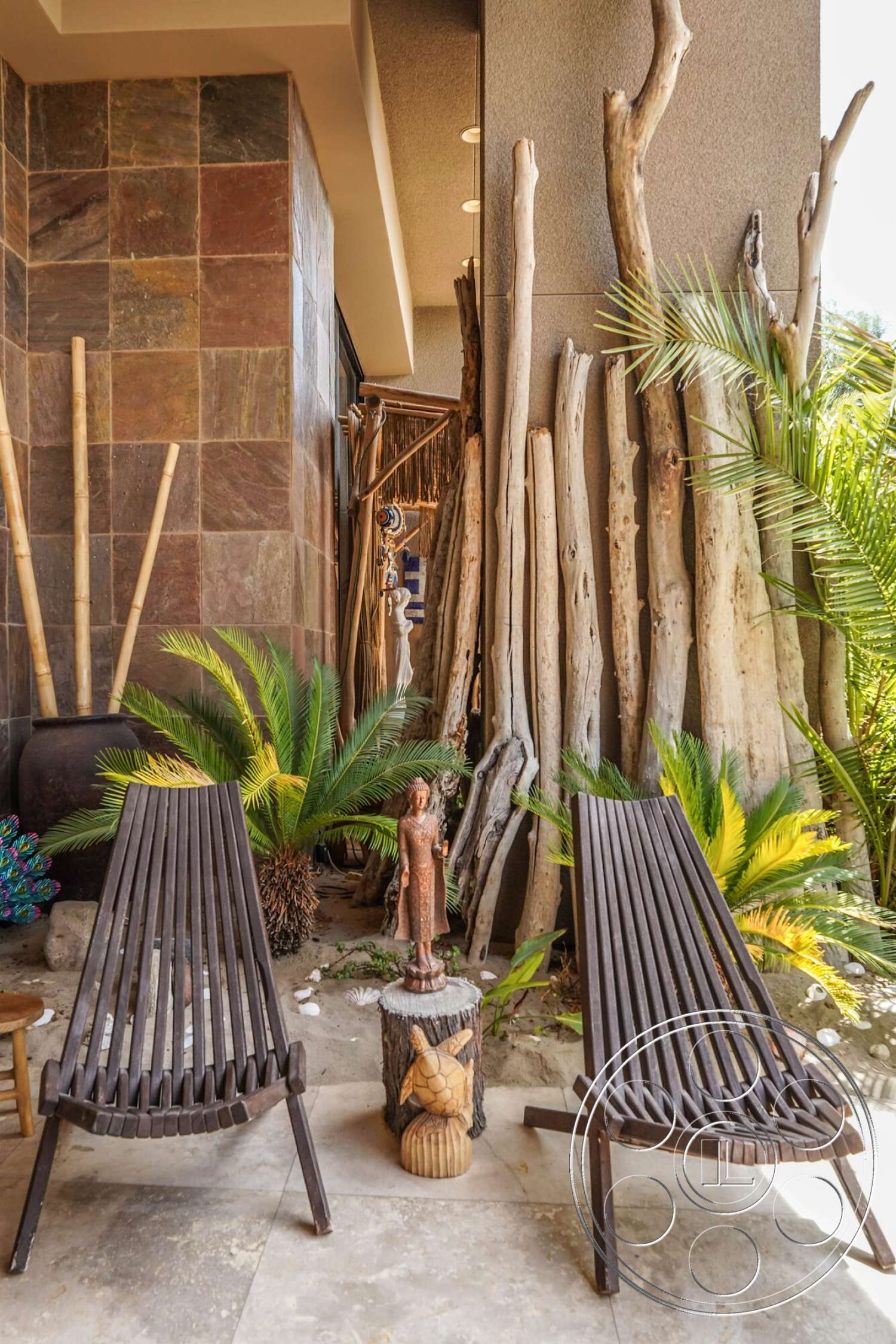 Rancho Mirage 4 - exterior, tropical landscaping, palm plants, wooden lounge chairs, smooth concrete floor, slate stone feature wall, natural wood tree branches, hand-carved wooden sculpture, decorative garden figurine, sandstone patio area