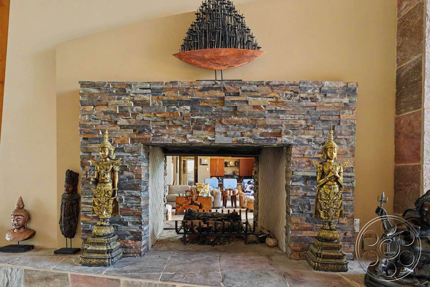 Rancho Mirage 4 - artistic wall decor, wood ceiling beams, neutral painted walls, stone fireplace surround, stacked stone wall, polished stone hearth, decorative golden sculptures, open living area view