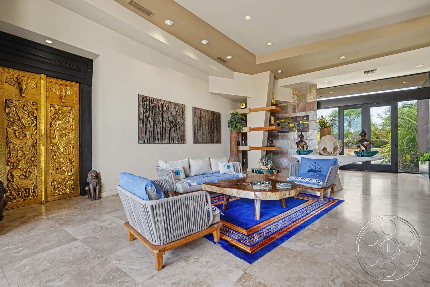 Rancho Mirage 4 - textured wall art, modern light fixtures, decorative sculptures, cream marble flooring, natural wood coffee table, neutral painted walls, floor-to-ceiling glass doors, indoor plant accents, light gray upholstered sofa, gold ornate front doors, blue and gold area rug, open shelving with plants