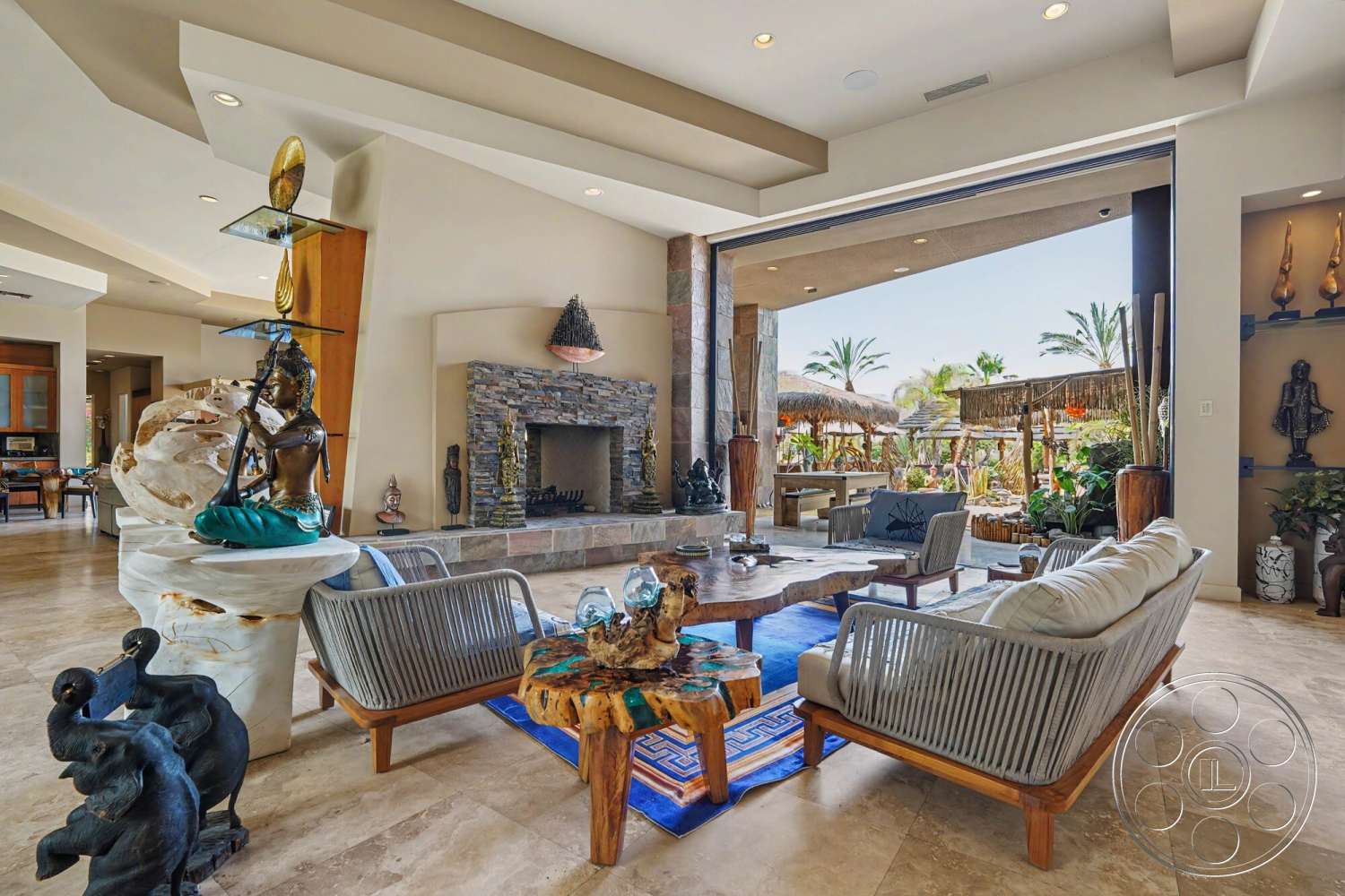 Rancho Mirage 4 - decorative area rug, open floor plan, outdoor seating area, decorative sculptures, lush landscaping, large sliding glass doors, natural wood coffee table, wood beam ceiling, stone fireplace wall, marble floor tiles, exposed stone accent wall, tropical outdoor setting, textured cream walls, modern rattan seating