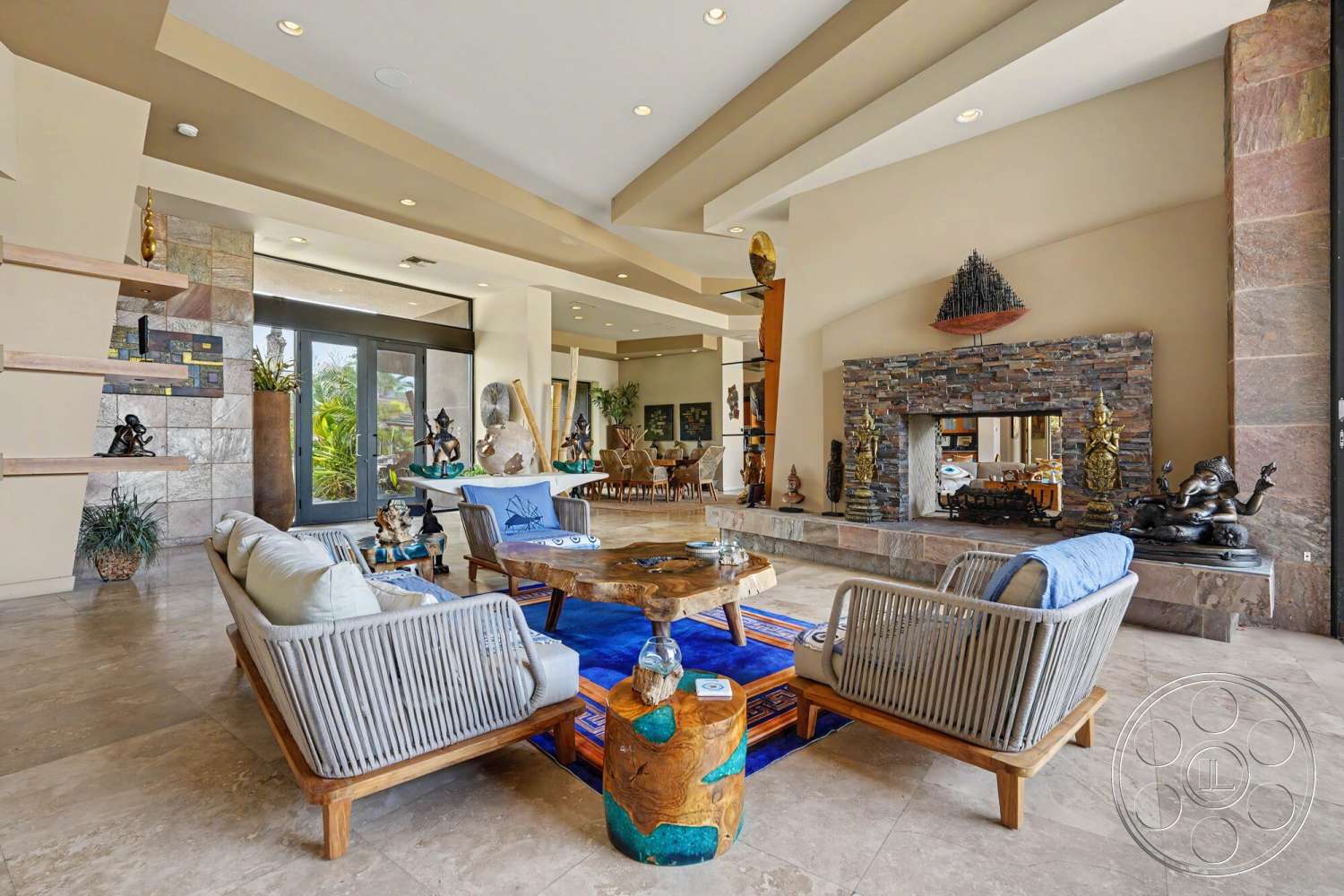 Rancho Mirage 4 - natural light, textured wall art, open floor plan, modern furniture, sliding glass doors, decorative sculptures, large glass doors, vaulted ceiling, marble flooring, dark wood shelving, stone feature wall, stone fireplace surround, coffered ceiling details, tropical plant accents