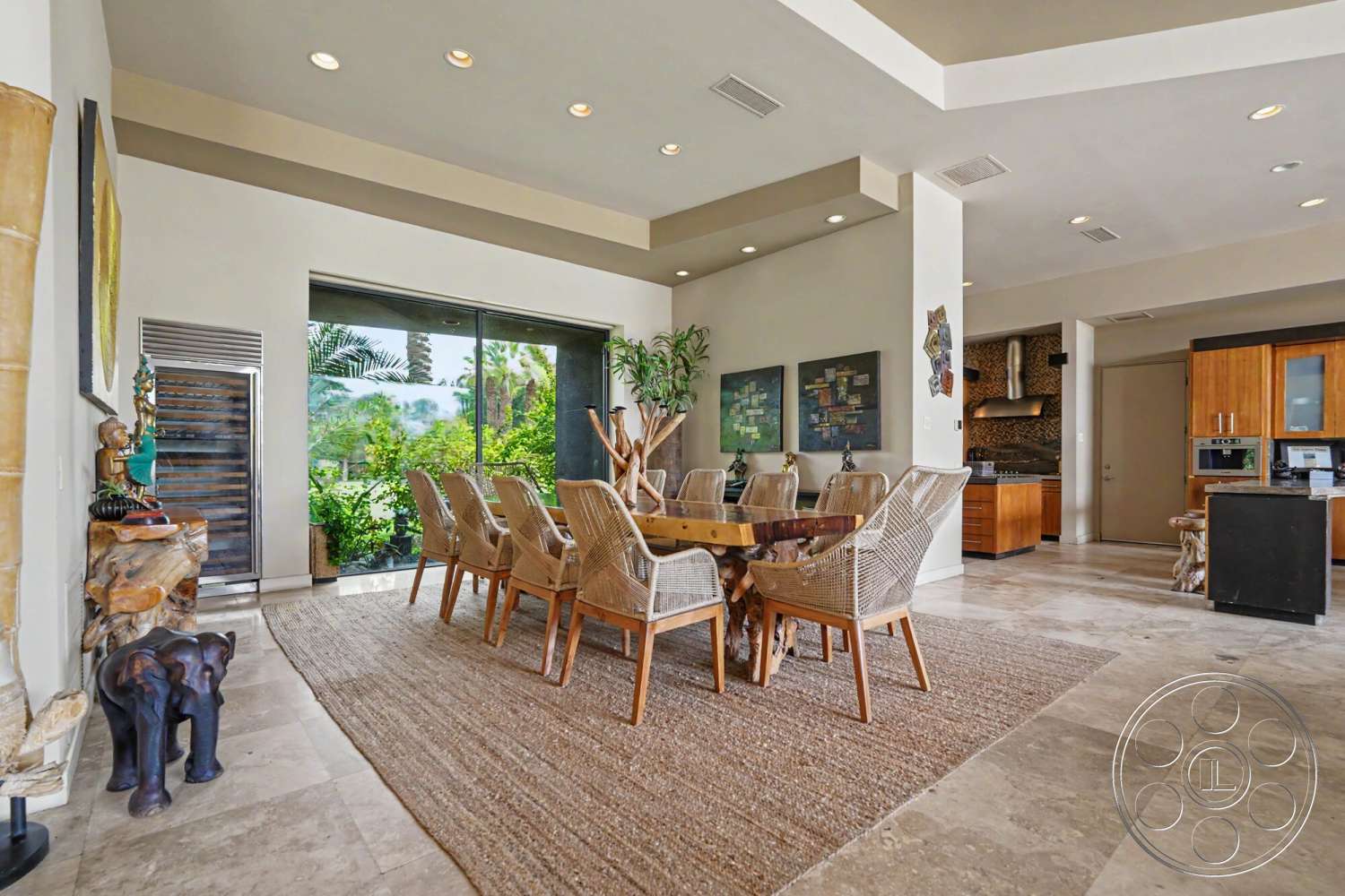 Rancho Mirage 4 - textured wall art, indoor plants, open floor plan, vaulted ceiling, natural stone flooring, wooden countertop, rectangular dining table, woven dining chairs, ceiling recessed lighting, smooth painted walls, expansive glass sliding doors, modern kitchen cabinets, jute area rug