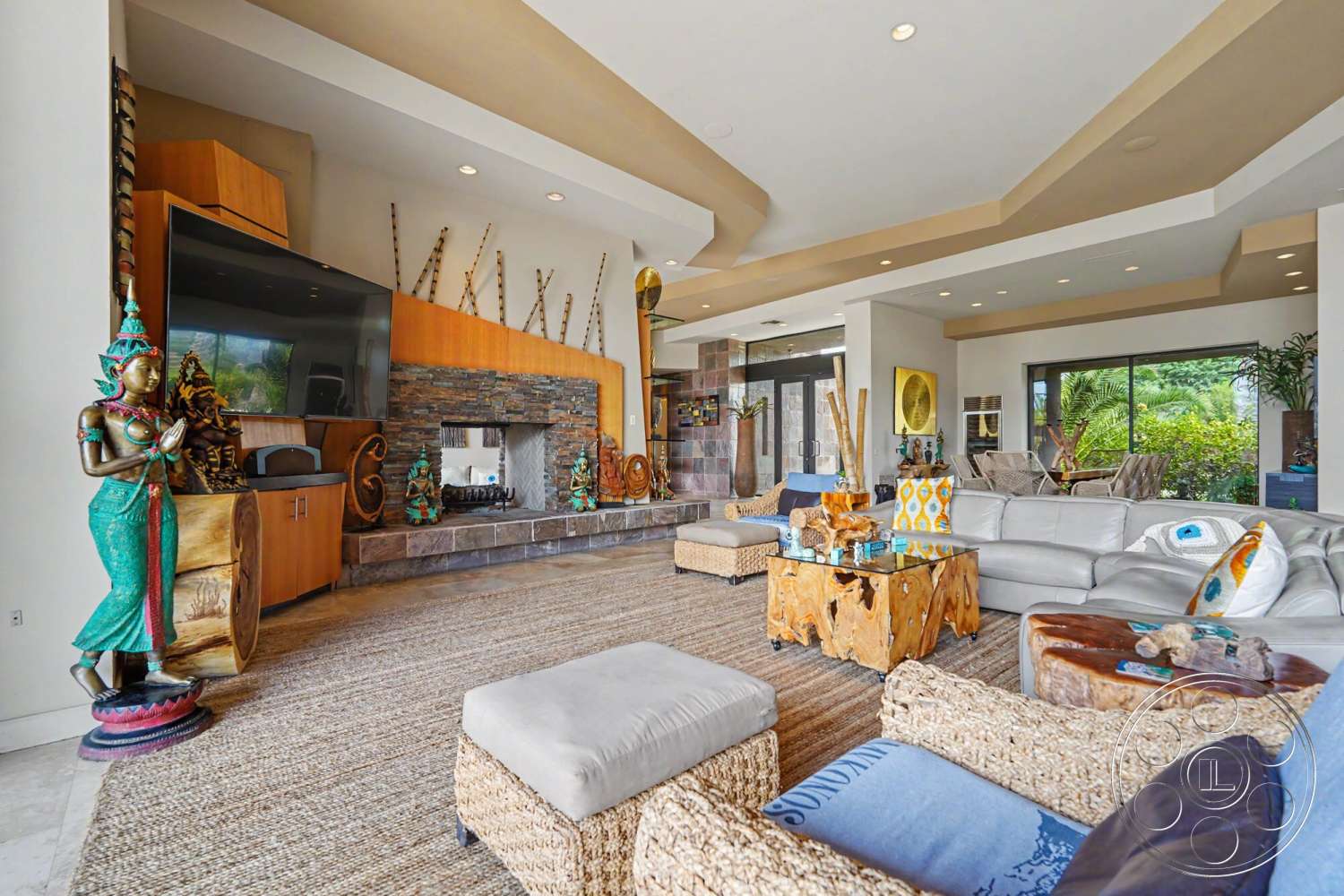 Rancho Mirage 4 - open floor plan, wood cabinetry, artistic wall decor, modern lighting fixtures, woven area rug, textured plaster walls, exposed wood ceiling, tropical plant decor, natural stone fireplace surround, glass windows with outdoor view, neutral colored furniture, decorative wooden accent table