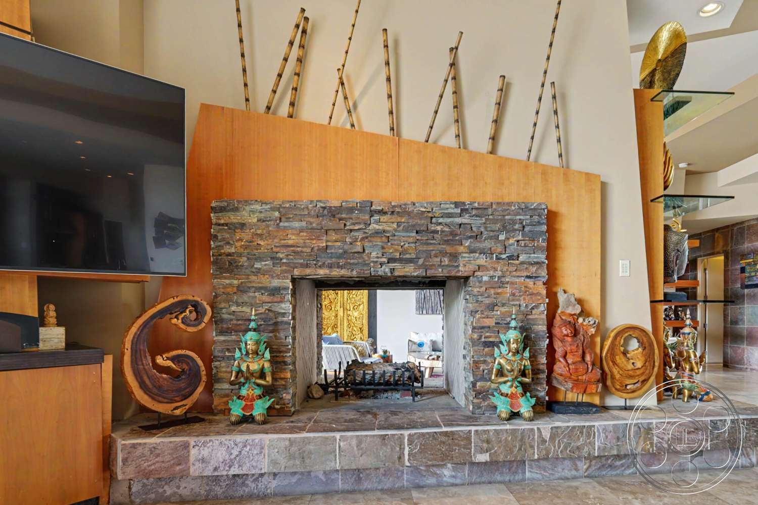 Rancho Mirage 4 - decorative sculptures, dark hardwood flooring, wood accent wall, modern art decor, contemporary living room design, mounted flat-screen television, stacked stone fireplace surround, exposed wooden display shelves, natural stone mantel