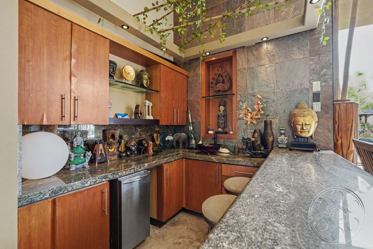 Rancho Mirage 4 - indoor plants, wood cabinetry, open shelving, bar seating area, decorative sculptures, granite countertop, under-cabinet lighting, polished stone backsplash, natural stone wall treatment, stainless steel fridge, unique decorative artifacts