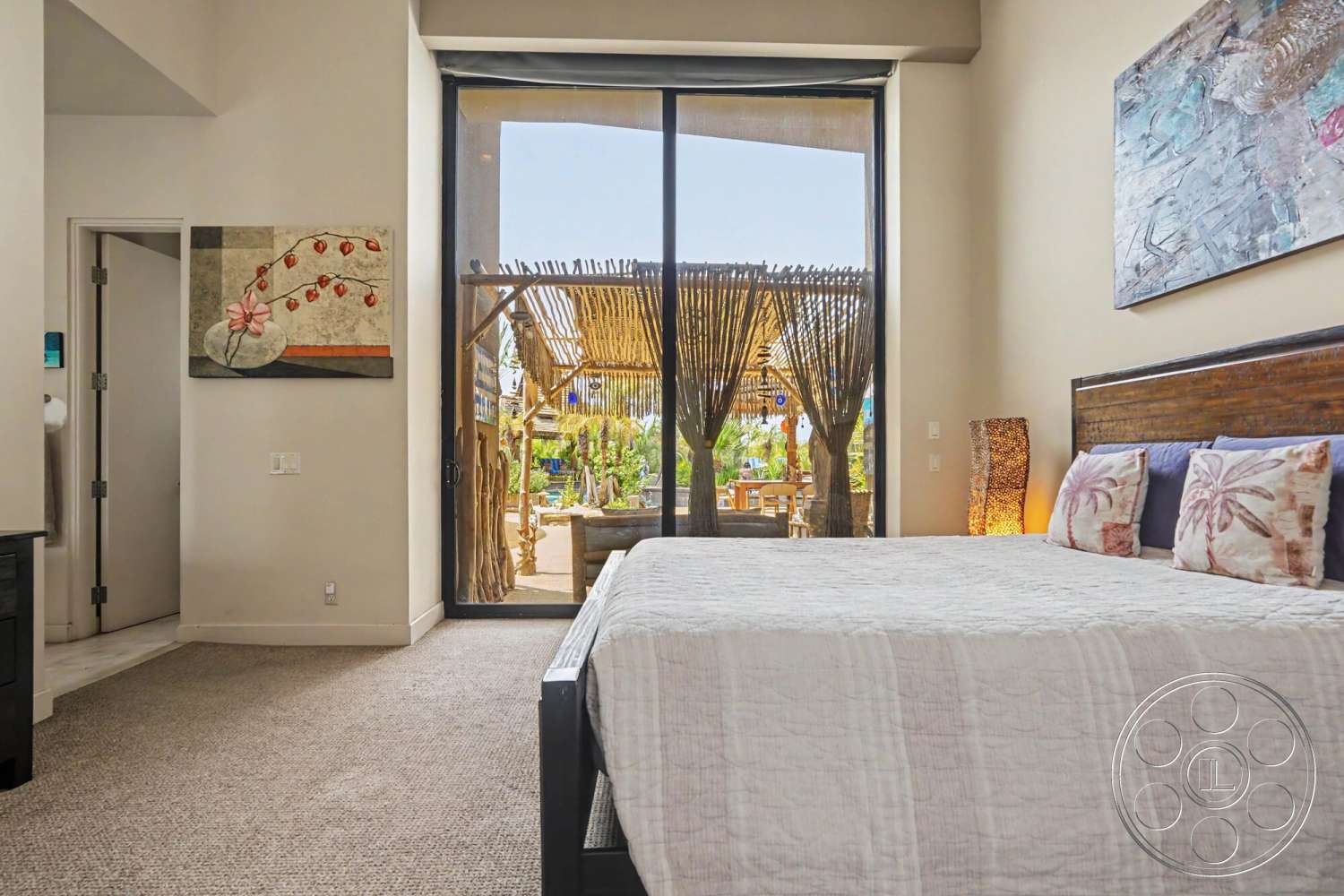 Rancho Mirage 4 - textured wall art, light beige wall color, interior bedroom, minimalist room design, contemporary art decor, dark wood bed frame, natural light exposure, floor-to-ceiling glass doors, carpet bedroom flooring, throw pillows with floral patterns, open view to outdoor patio