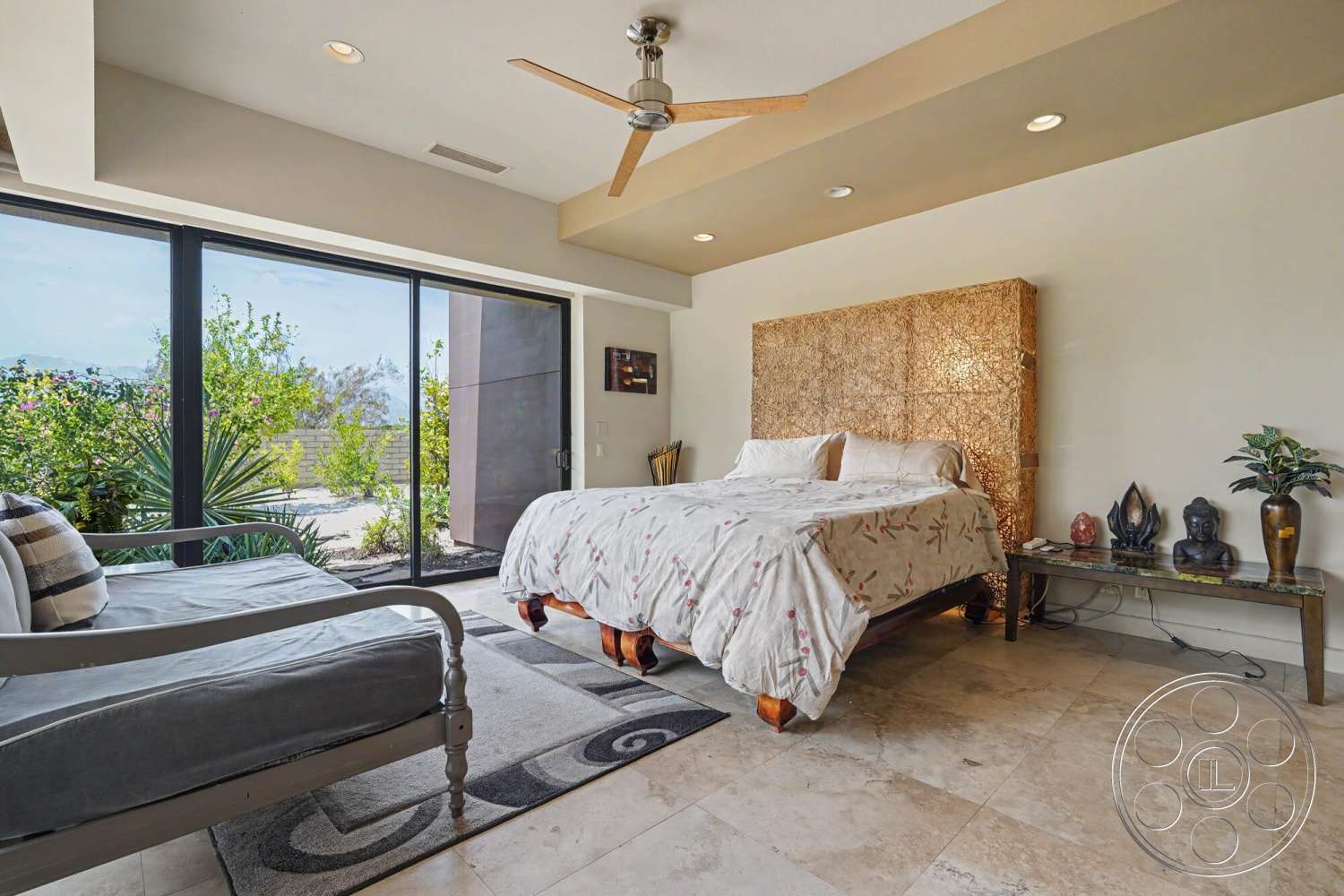 Rancho Mirage 4 - neutral color palette, clean lines, textured wall finish, soft area rug, king-sized bed, glass patio doors, woven headboard, large window view, minimalist bedside table, tile bedroom flooring, swivel ceiling fan, modern upholstered chair