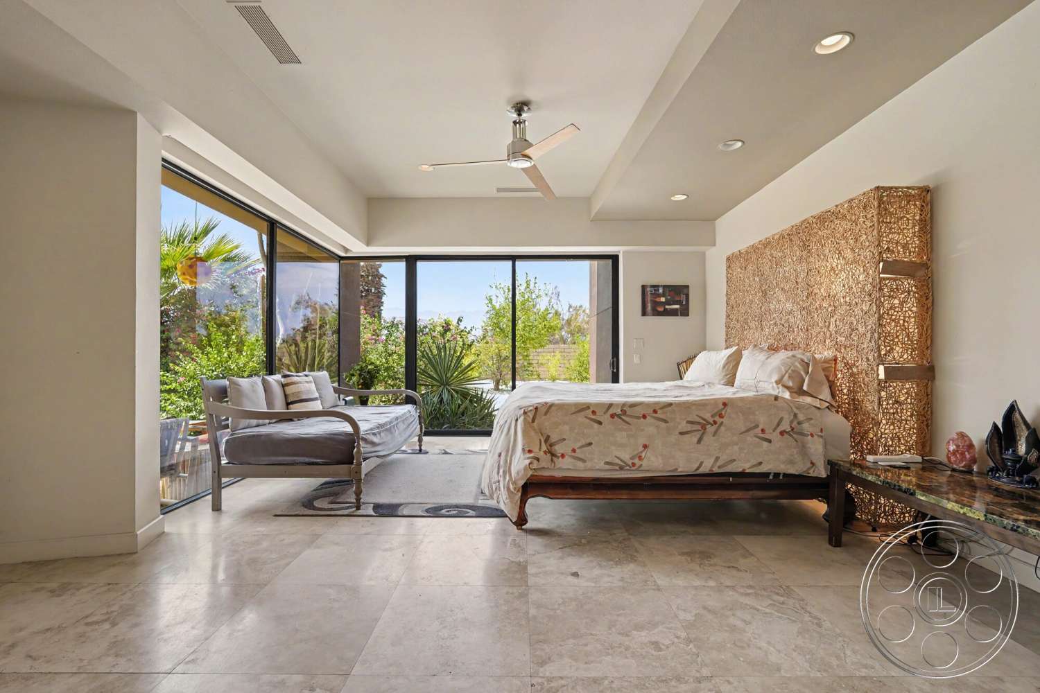 Rancho Mirage 4 - neutral color palette, minimalist design, contemporary decor, large glass sliding doors, seating area, floor-to-ceiling windows, modern ceiling fan, natural light flooded space, spacious open layout, tropical garden view, marble bedroom flooring, decorative side table, woven headboard wall