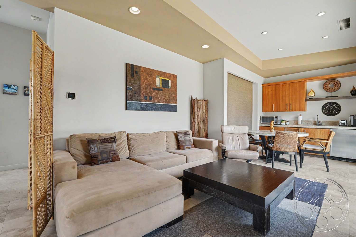Rancho Mirage 4 - decorative wall art, open concept living space, textured plaster walls, polished tile flooring, beige sectional sofa, dark wood coffee table, recessed ceiling lights, modern dining area, wooden kitchen cabinets, woven room divider