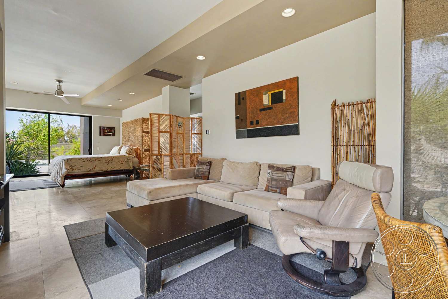 Rancho Mirage 4 - natural light, minimalist design, textured wall art, open floor plan, potted plants, sectional sofa, king-sized bed, dark wood coffee table, large sliding glass doors, modern ceiling fan, stone tile flooring, white painted walls, neutral bedding, bamboo room divider