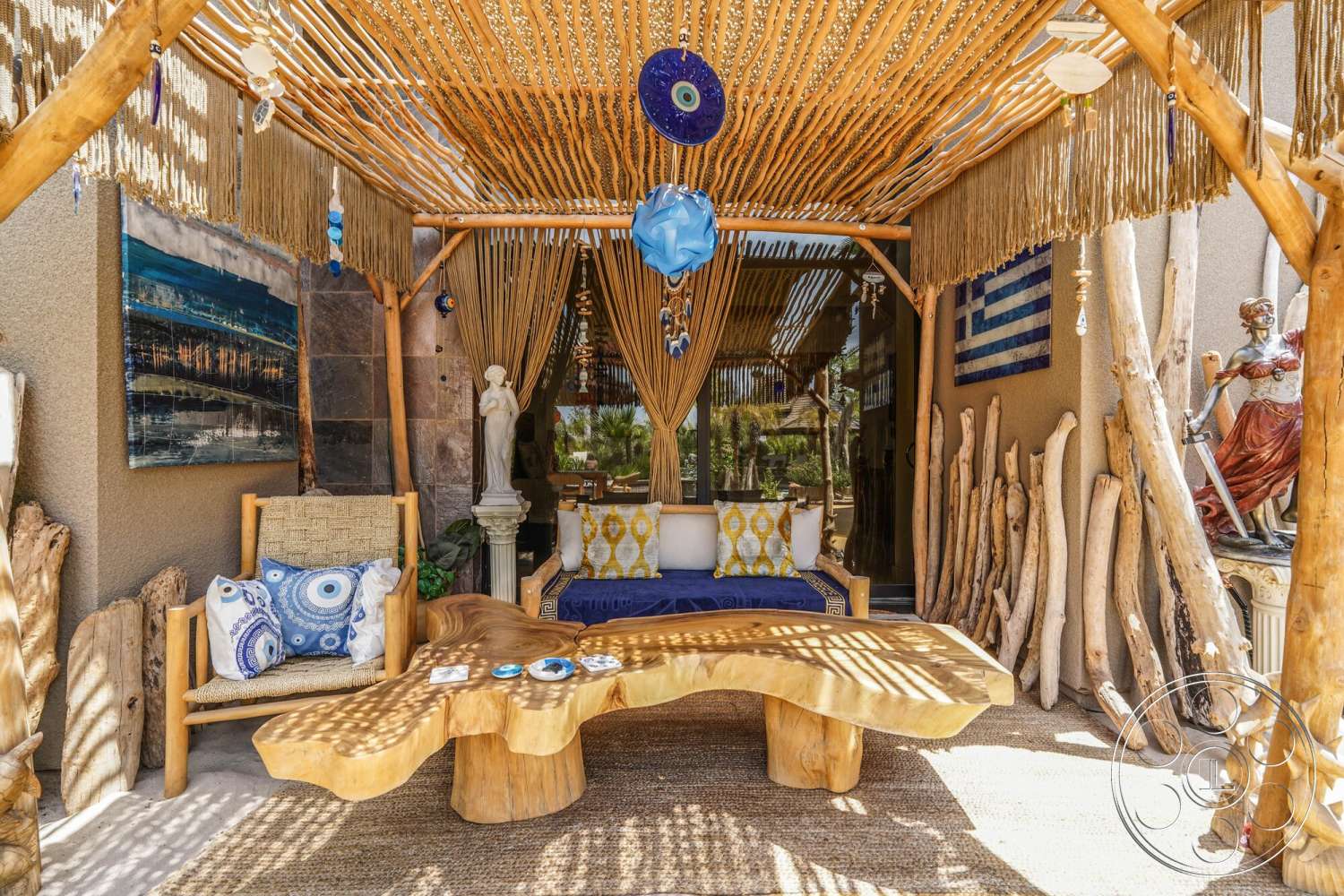 Rancho Mirage 4 - exterior, outdoor seating area, decorative sculptures, woven area rug, tropical landscaping, wooden pergola, textured plaster walls, natural wood furniture, patterned throw pillows, stone feature wall, bamboo privacy screen, statue decor, painted wall art, woven straw roof, live edge wooden table, blue ceramic accents