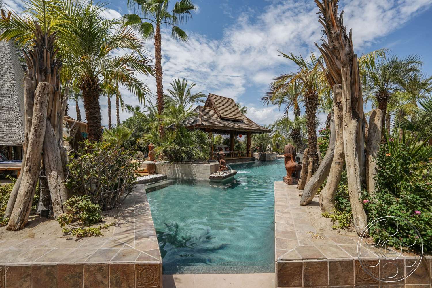 Rancho Mirage 4 - exterior, lush tropical landscaping, rectangular pool, tropical palm trees setting, wooden gazebo structure, weathered wood accents, paver stone patio flooring, decorative stone sculptures, natural stone pool edges, ceramic tile details