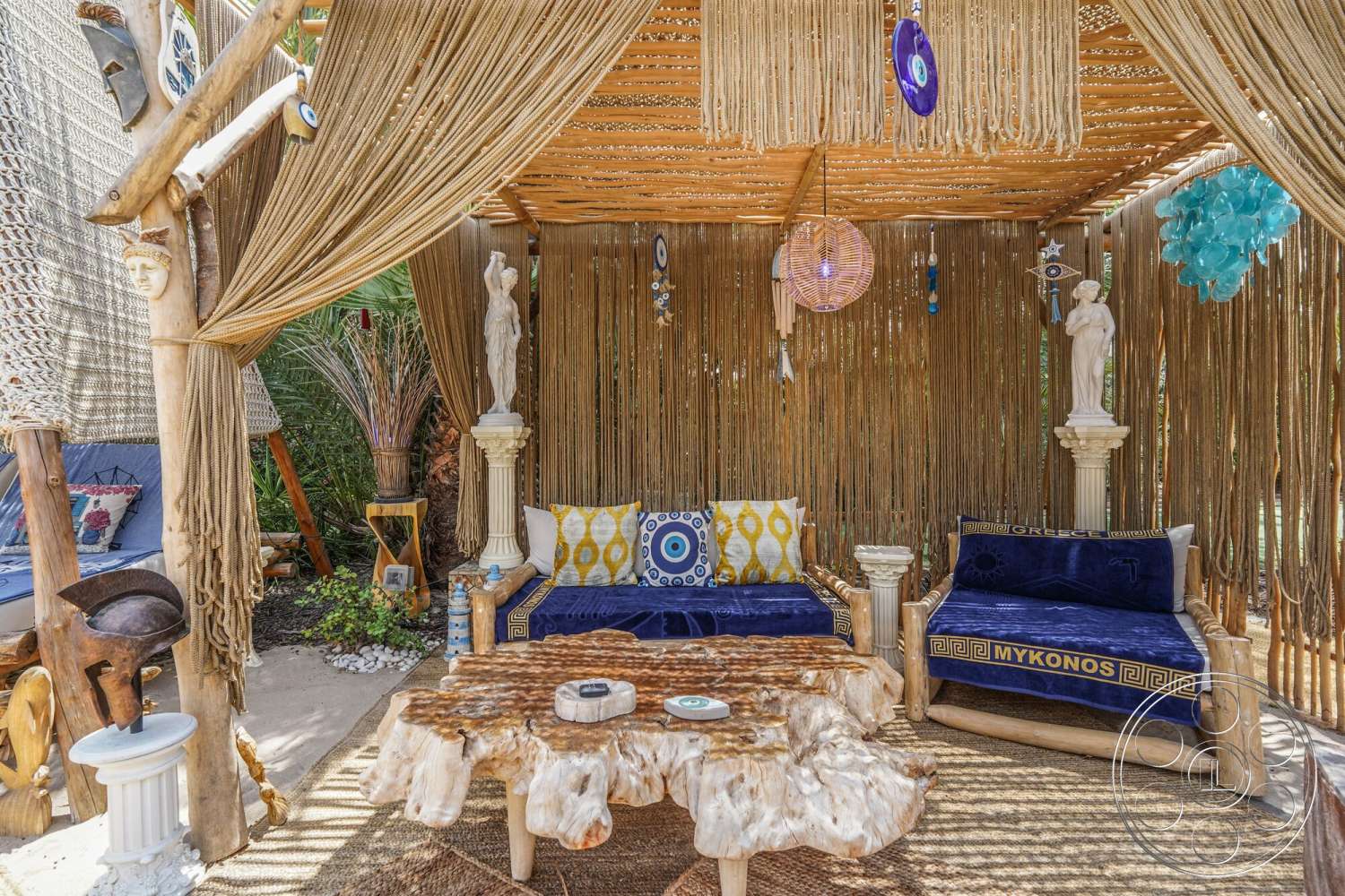 Rancho Mirage 4 - natural wood furniture, exterior seating area, textured fabric cushions, decorative figurines, tropical plant landscaping, stone garden accents, pendant light fixtures, macrame wall hanging, earth-toned area rug, live edge wood coffee table, bamboo ceiling, woven fabric wall decor, colonnaded support pillars