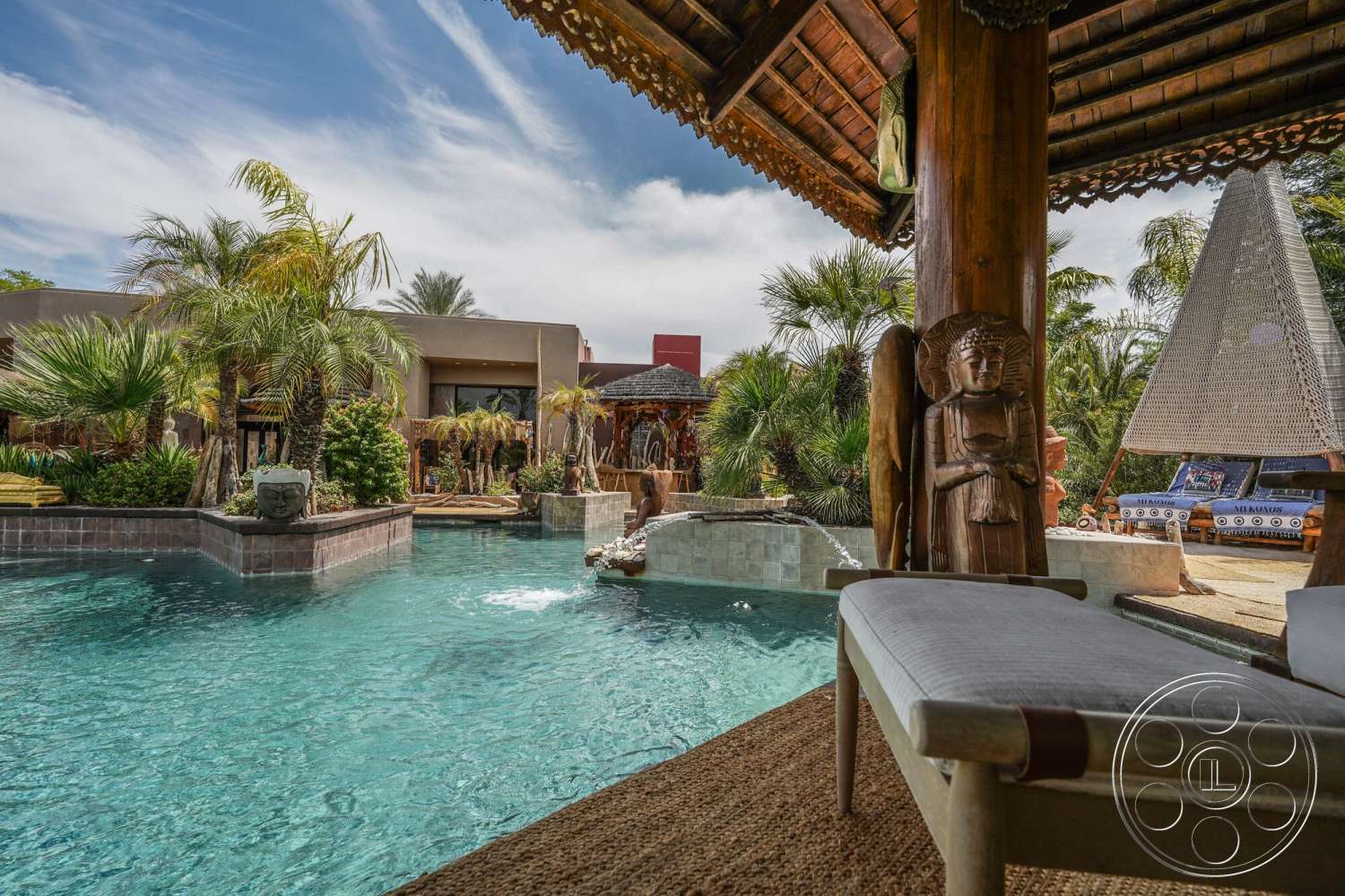 Rancho Mirage 4 - exterior, stucco walls, infinity pool, natural stone pool border, wooden thatched roof pavilion, bamboo loungers, palms and tropical landscaping, textured stone pathways, carved wooden sculptures, woven take of patio furniture, textured grass patches