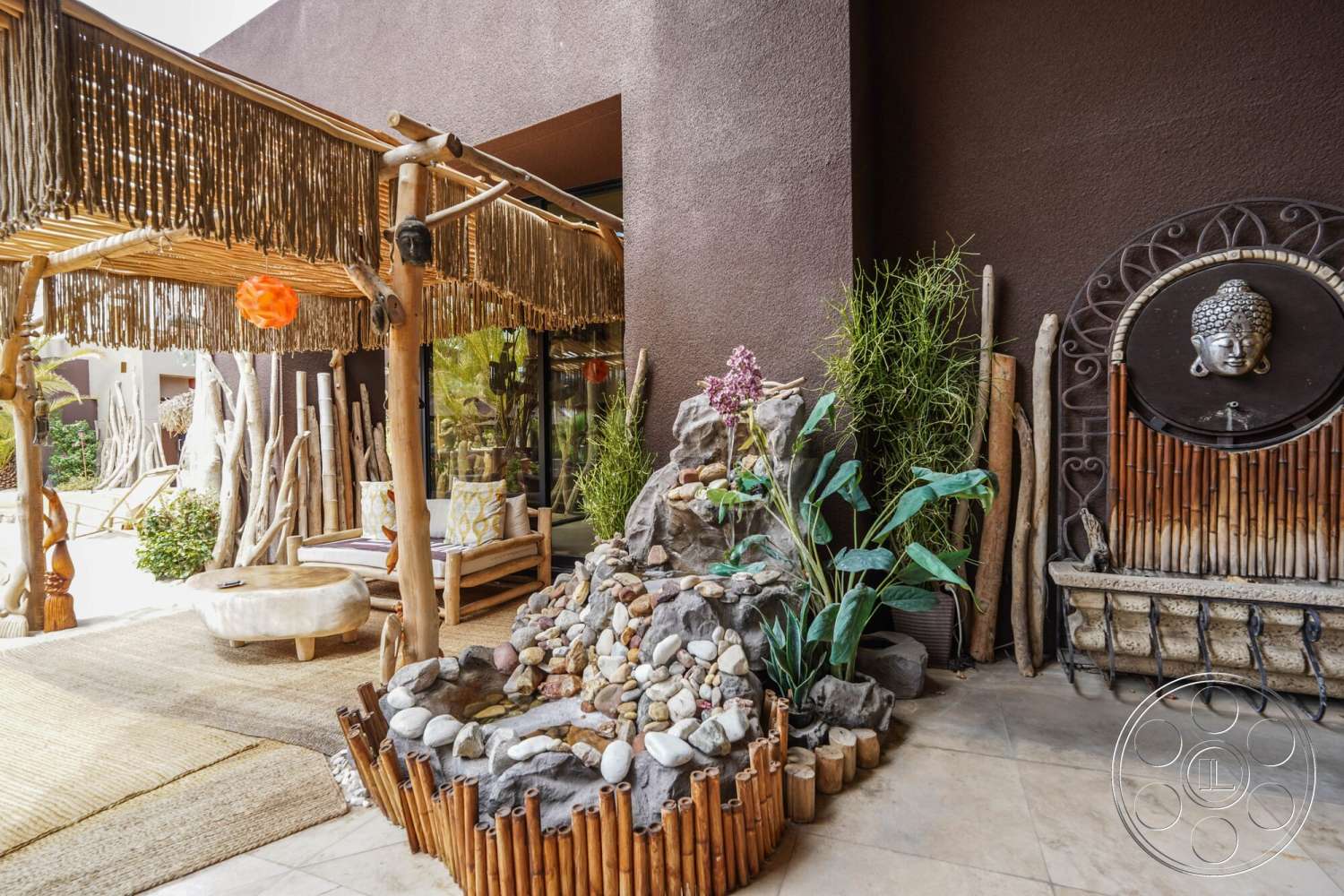 Rancho Mirage 4 - concrete flooring, terra cotta planters, woven natural fiber rug, green tropical plants, interior courtyard setting, bamboo patio cover, thatch roof shade structure, exposed rock water feature, smooth pebbled stone border, wooden siesta chairs, decorative bamboo wall, meditative outdoor area