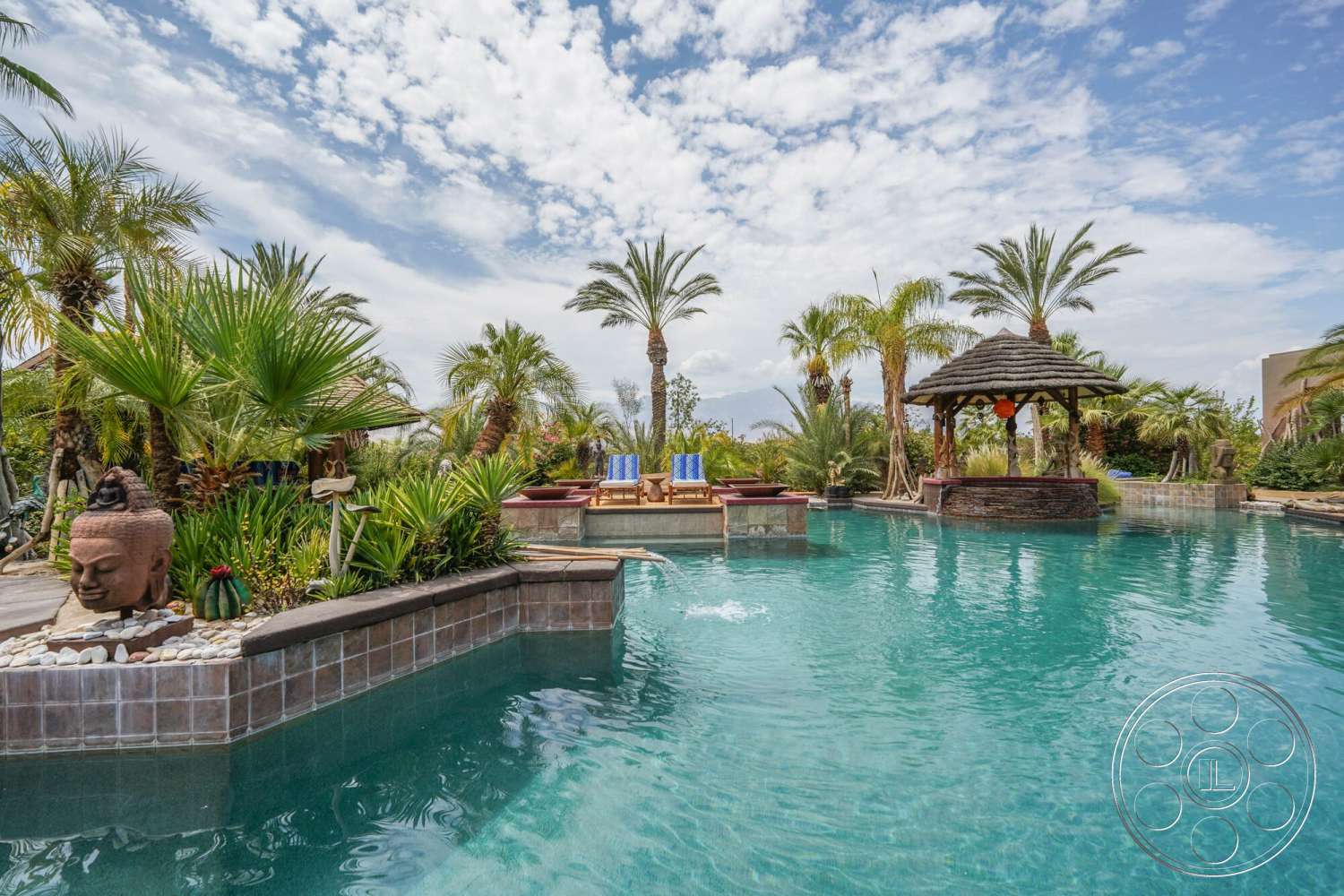 Rancho Mirage 4 - exterior, water feature, spa area, decorative stone accents, stone patio flooring, landscape with palm trees, tropical garden setting, tile pool surround, luxury infinity pool, thatched gazebo structure, colorful lounge chairs