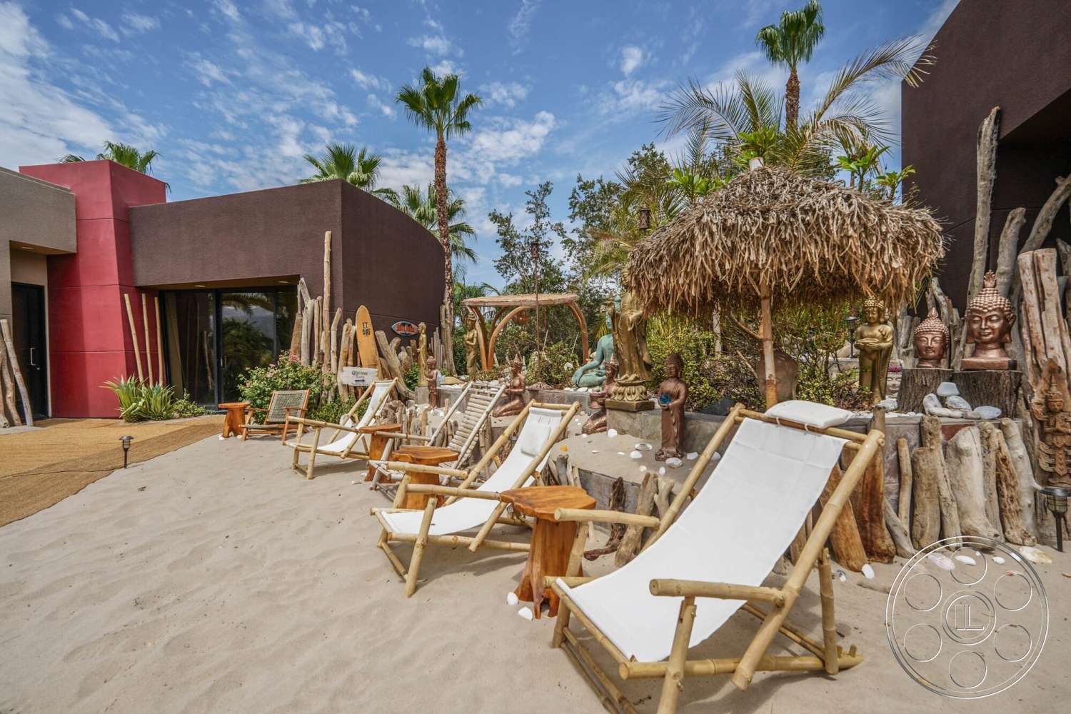 Rancho Mirage 4 - exterior, palm trees, red accent wall, tropical landscaping, thatched roof gazebo, stucco walls, flat roof design, open courtyard layout, decorative stone sculptures, sand patio floor, bamboo lounge chairs, wooden garden decor