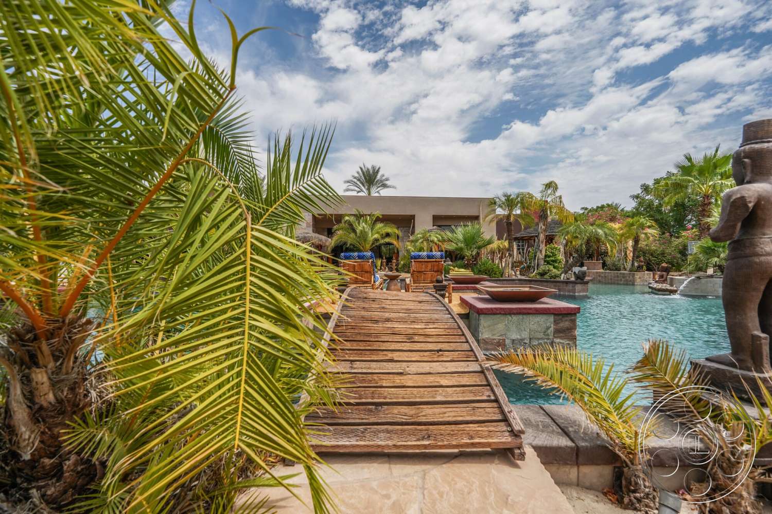 Rancho Mirage 4 - exterior, natural stone elements, palm trees, outdoor seating area, water feature, rectangular swimming pool, tropical landscaping, wooden walkway, stone pool deck, concrete pool border, slate stone retaining wall, skyview with clouds