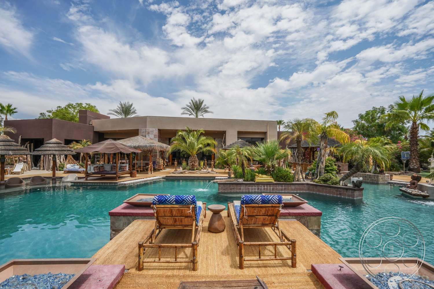 Rancho Mirage 4 - exterior, palm trees, outdoor seating area, wood decking, modern architectural style, tropical landscaping, infinity pool, stone pool deck, stucco exterior walls, rectangular patio, desert home, thatched-roof cabana, wicker lounge chairs, tanned wood pergola