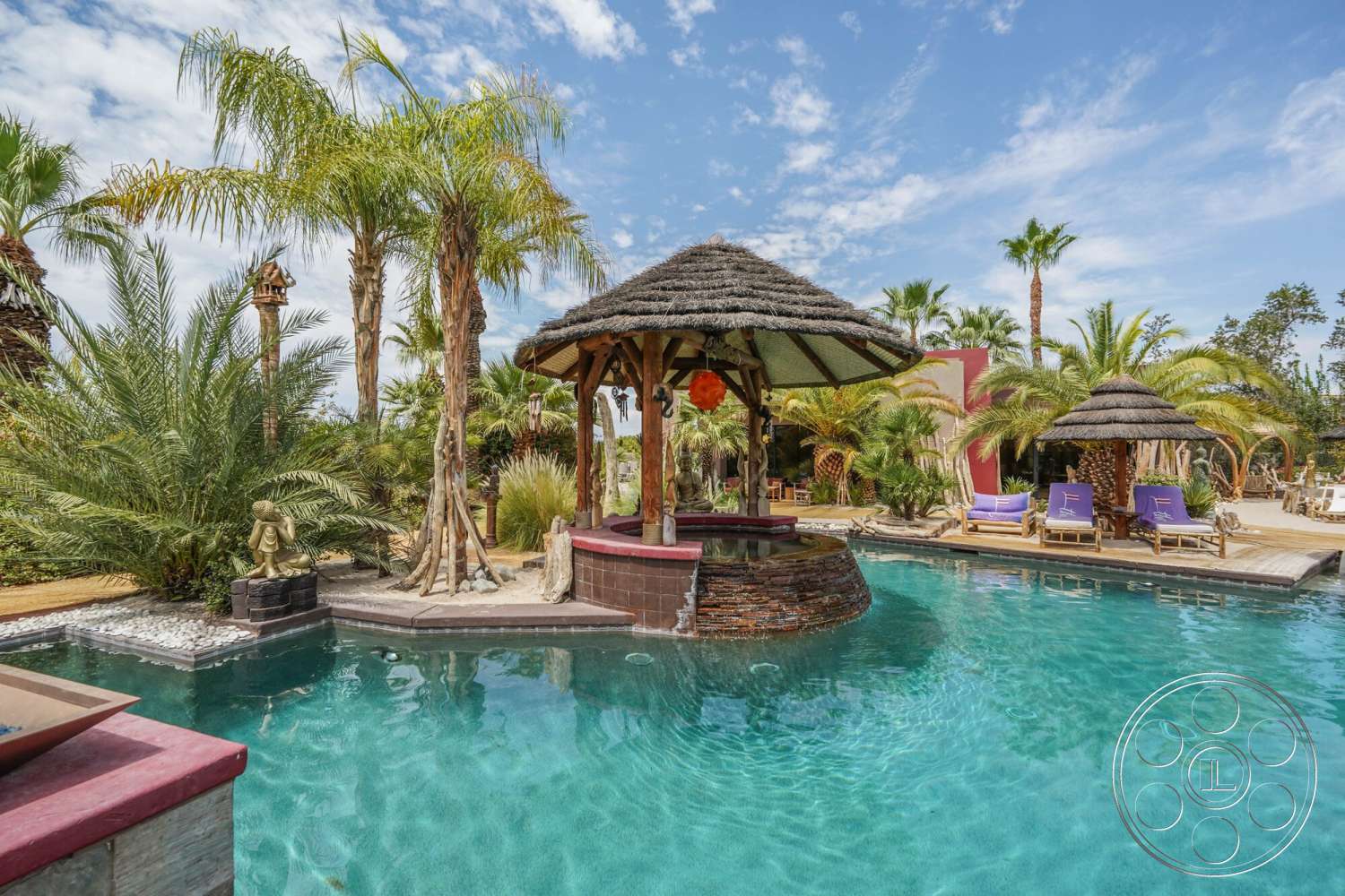 Rancho Mirage 4 - exterior, water feature, thatched roof gazebo, tropical landscape, infinity pool, outdoor lounge chairs, stone pool border, wooden pool deck, decorative stone features, colorful accent walls, palms surrounding pool, sandstone paving