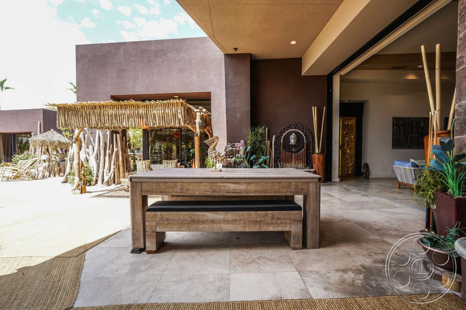 Rancho Mirage 4 - exterior, palm trees, natural wood accents, wood dining table, sliding glass doors, floor-to-ceiling windows, modern architectural style, stucco walls, concrete patio flooring, thatched roof pergola, woven grass outdoor rug