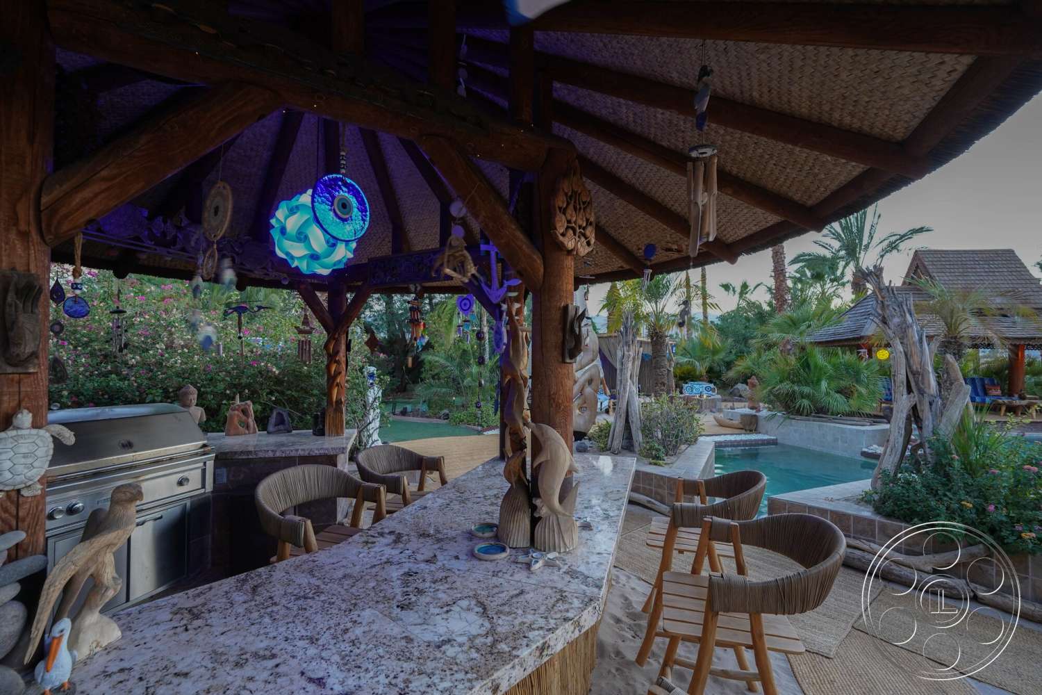 Rancho Mirage 4 - exterior, natural stone accents, palm trees, woven bar stools, decorative sculptures, swimming pool, outdoor dining area, tropical landscaping, open-air patio, stone pool deck, stainless steel outdoor grill, thatched roof structure, granite countertop bar, decorative wind chimes, wooden support posts, pathway pavers