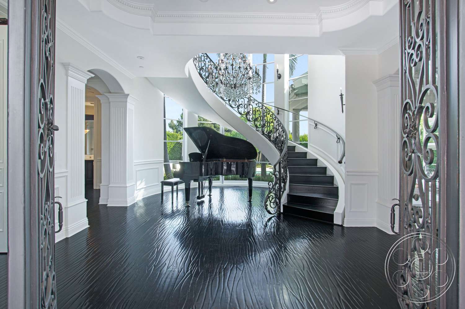 Medit 170 - floor-to-ceiling windows, arched doorways, ornate chandelier, curved staircase, black hardwood flooring, white painted walls, crown molding details, elegant foyer space, wrought iron door
