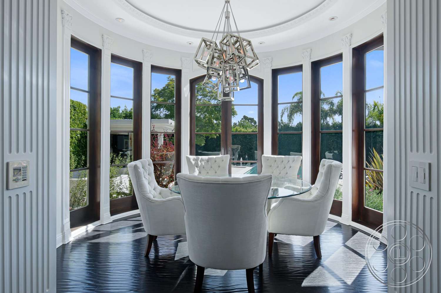 Medit 170 - modern chandelier, white paneling, round glass dining table, black hardwood flooring, crown molding details, tropical garden view, large bay windows, white upholstered dining chairs