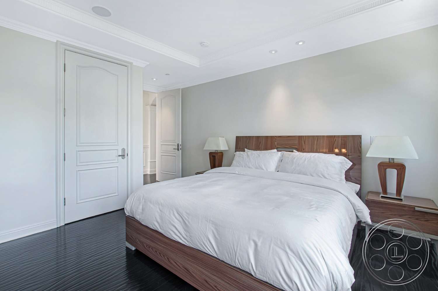 Medit 170 - white bedding, modern bedside lamps, recessed ceiling lights, dark hardwood bedroom floors, white painted walls, crown molding details, walnut wood bed frame, paneled white door
