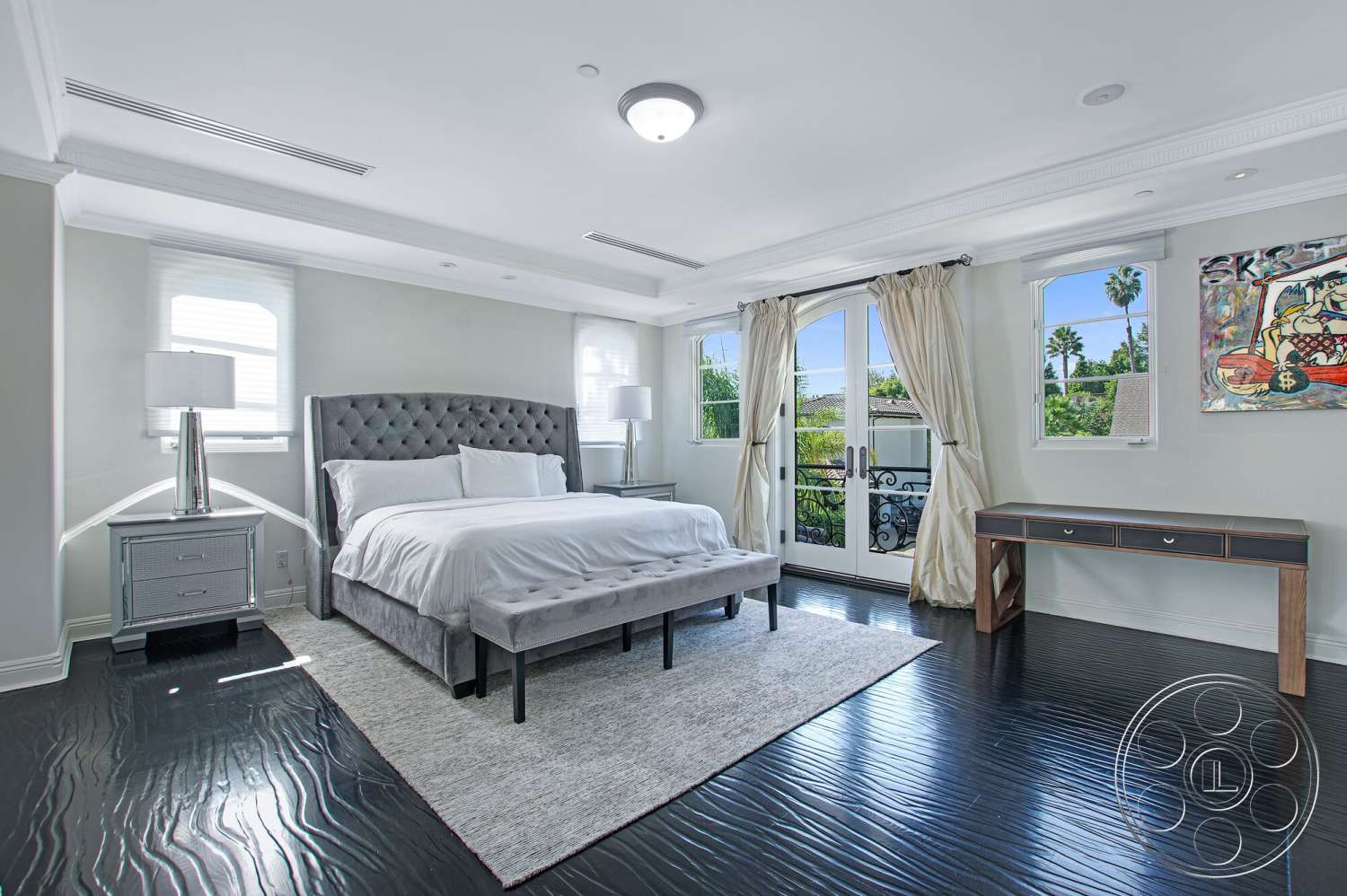 Medit 170 - gray upholstered bed, floor-to-ceiling windows, decorative wall art, white bedding, modern bedside lamps, white sheer curtains, light gray area rug, dark hardwood bedroom floors, glass window panes, framed artwork on wall, wood accent side table, white ceiling with crown molding, console table with drawer