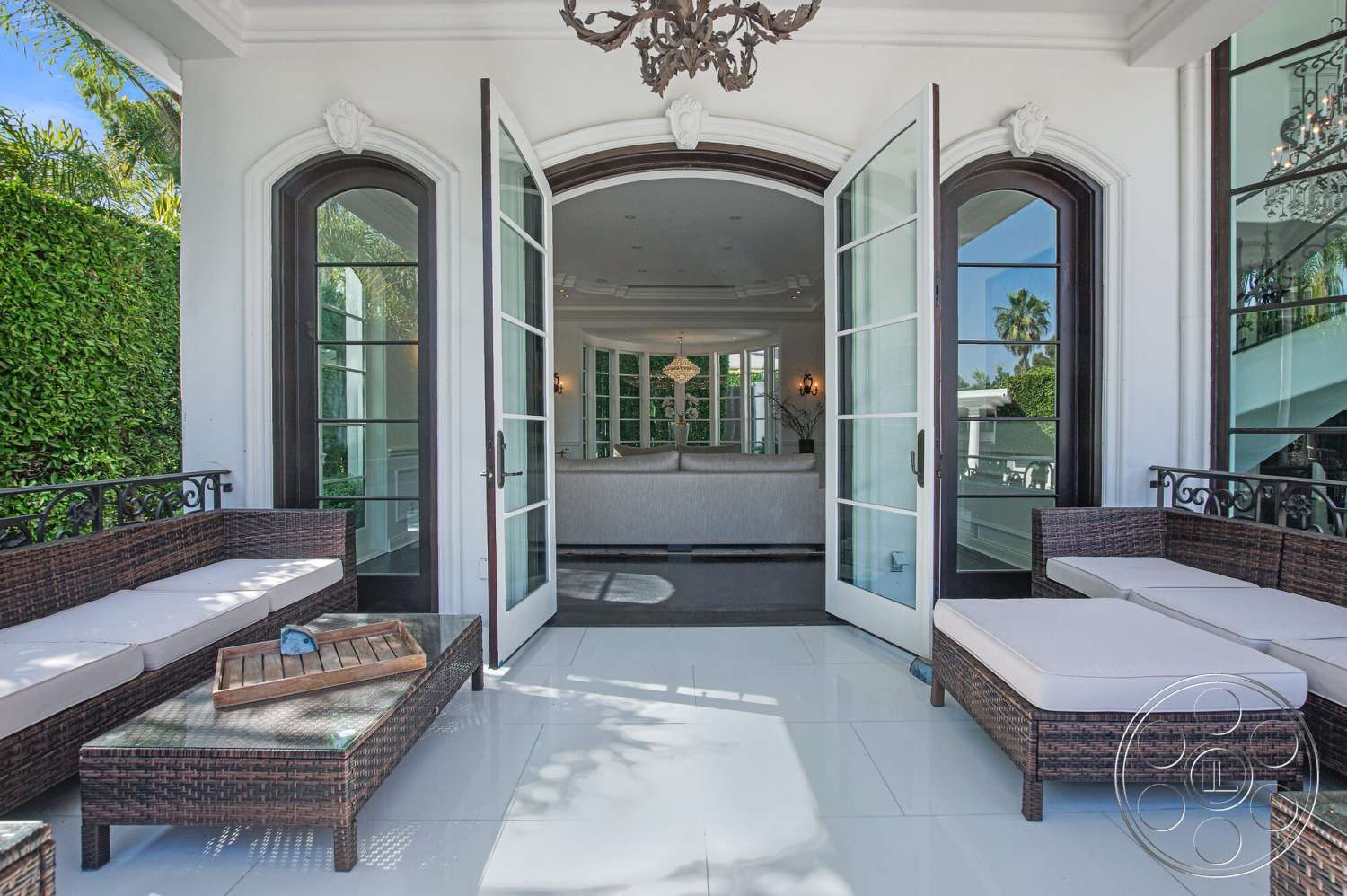 Medit 170 - natural light, open floor plan, outdoor living space, arched doorways, contemporary chandelier, dark wicker furniture, modern interior design, luxury outdoor seating area, palm tree landscaping, wrought iron railing details, white tiled floor, sliding glass French doors, green hedged privacy wall