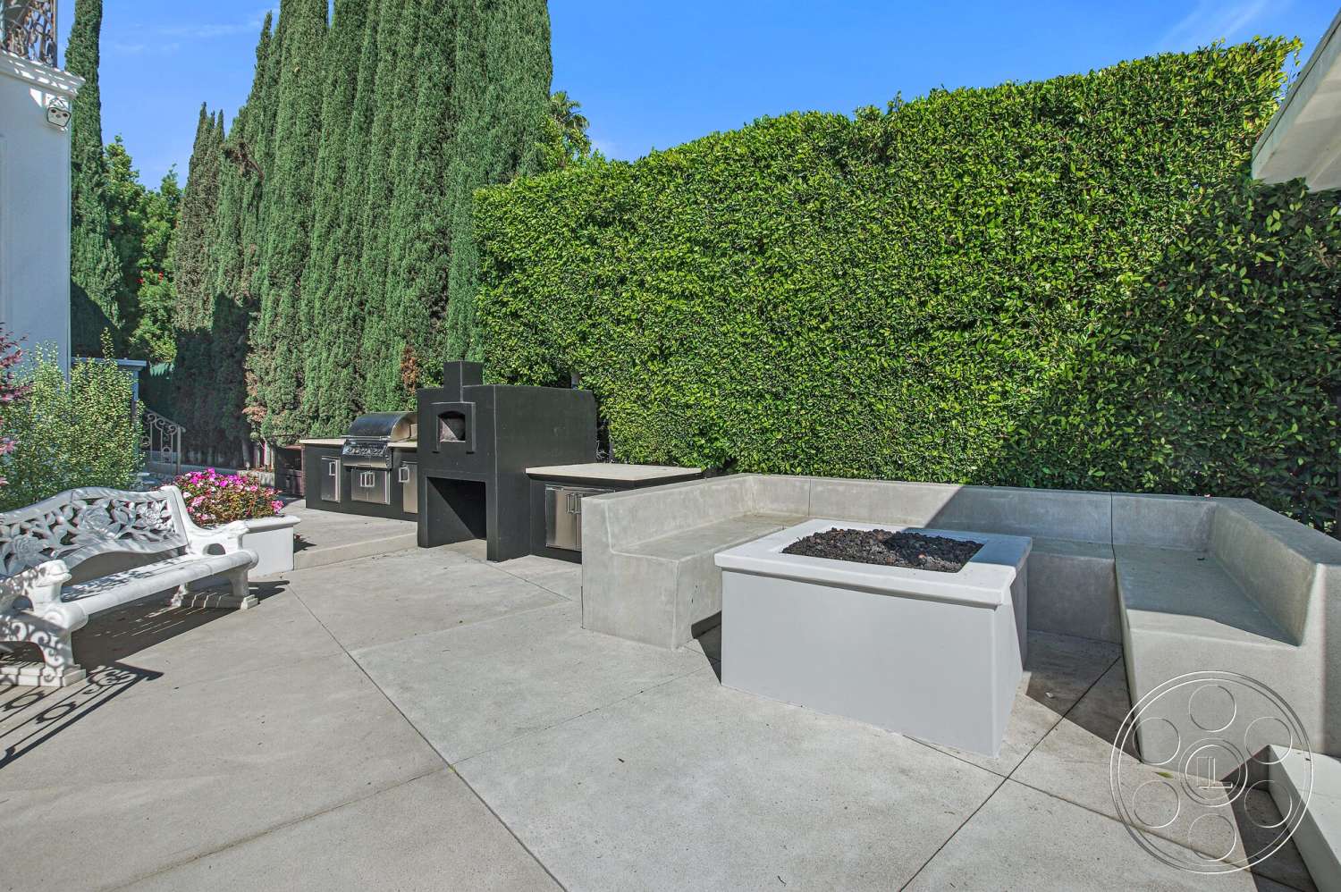 Medit 170 - exterior, lush green hedges, contemporary outdoor design, concrete patio flooring, stainless steel outdoor grill, concrete outdoor seating area, rectangular concrete fire pit table, decorative white bench