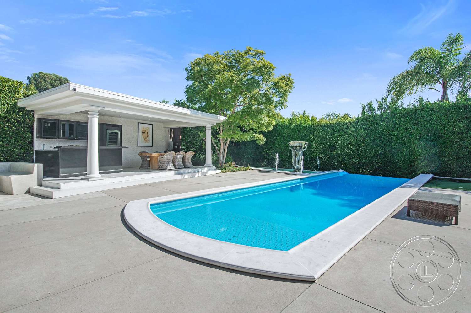 Medit 170 - exterior, landscaped garden, wooden dining table, woven outdoor chairs, water features, concrete pool deck, concrete patio floor, rectangular infinity pool, tall hedge privacy wall, stone outdoor kitchen, porch with columned roof