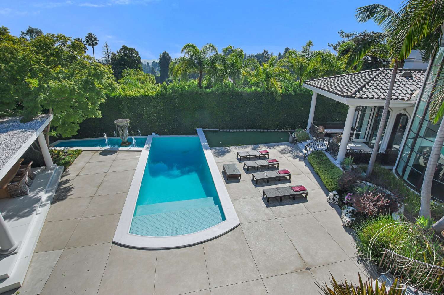 Medit 170 - outdoor seating area, metal railing, tiled roof, rectangular pool, sunny outdoor setting, concrete patio flooring, stucco exterior walls, brick garden border, stone water feature, lush palm landscaping, sun loungers with cushions, glass pool tile border, wall of dense greenery
