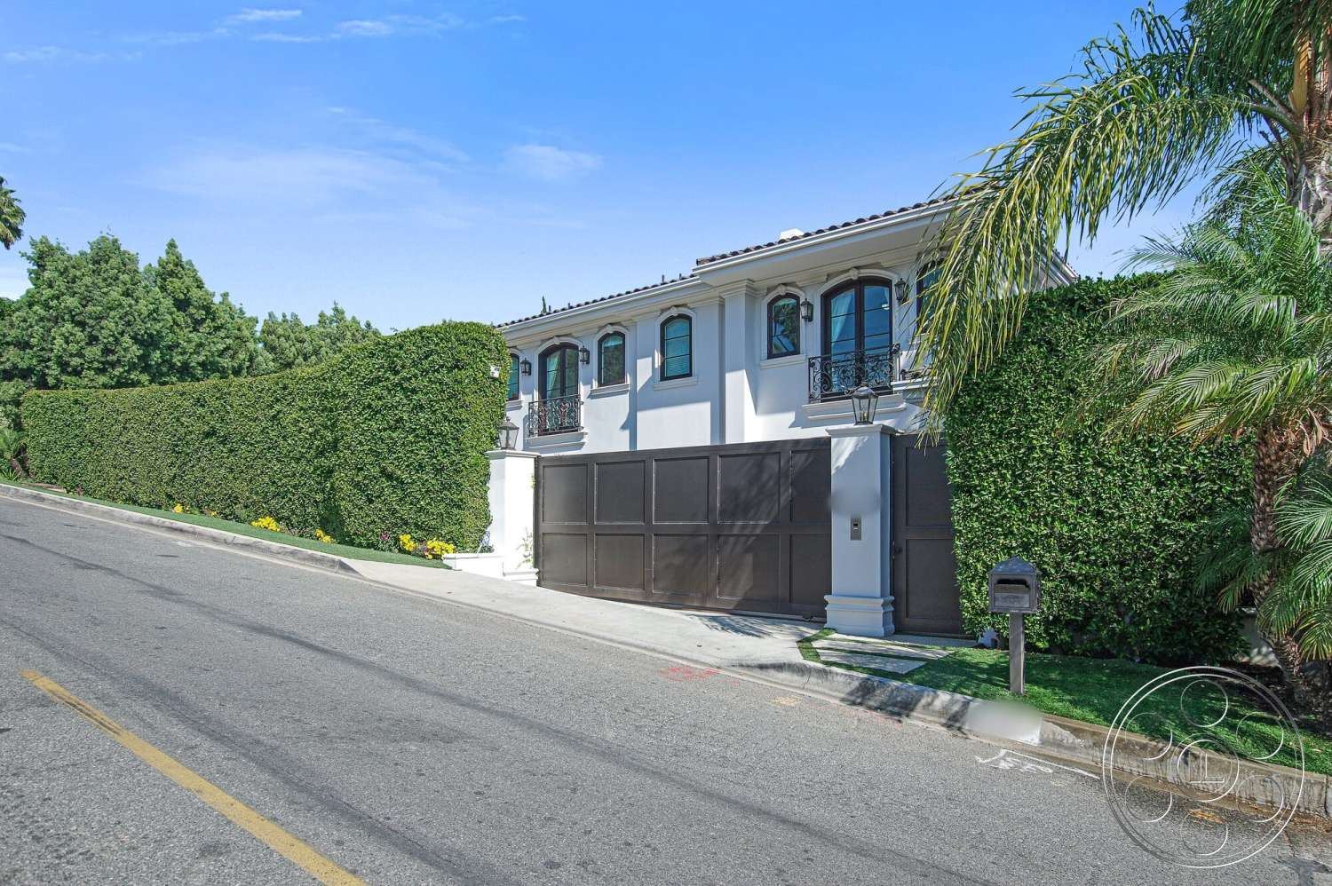 Medit 170 - exterior, paved driveway, sloped driveway, stucco walls, tropical palm trees, modern Mediterranean architecture, landscaped hedges, metal gate with wooden accents, arched windows with wrought iron railings