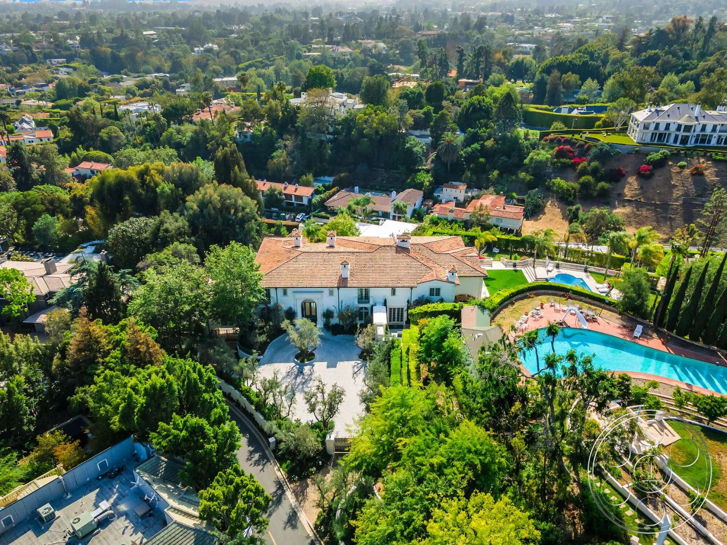 Medit 171 - exterior, white stucco walls, surrounding hillside, circular driveway, red clay tile roof, wooden patio furniture, stone pool deck, landscaped garden with mature trees, mediterranean-style home, large rectangular swimming pool, multi-level lawn terraces, city suburb setting
