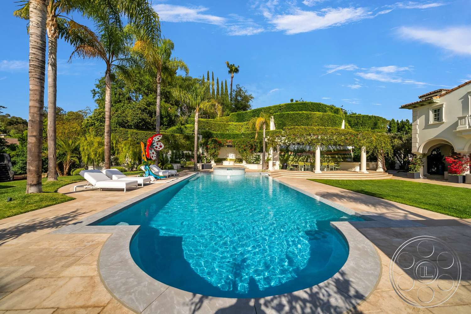 Medit 171 - exterior, palm trees, rectangular swimming pool, white lounge chairs, lush green landscaping, stone patio flooring, concrete pool border, colorful outdoor art, arbor with climbing plants, traditional Mediterranean architecture